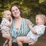 A joyful mother embraces her two sons in a lush park setting, capturing a sweet family moment.