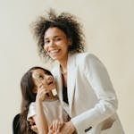 Smiling mother and daughter sharing a joyful moment, embracing in stylish outfits indoors.