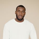 Stylish portrait of a confident man in a white sweater against a neutral background.